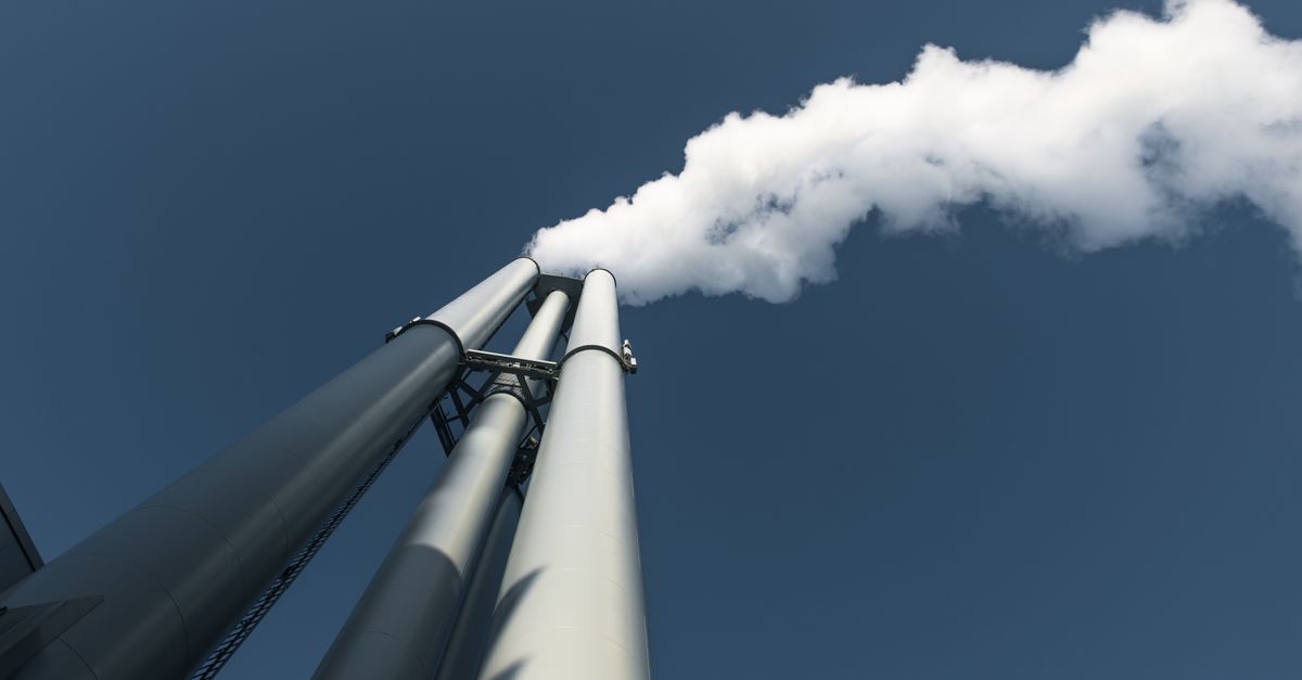 Upward view of factory chimneys releasing smoke into clear sky in Hamburg.